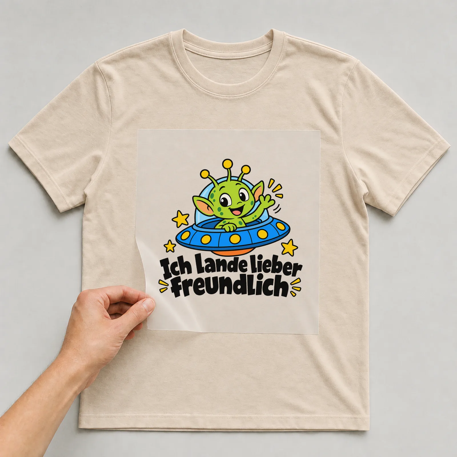 Bügelbild „Ich lande lieber freundlich“ auf beigem T-Shirt, Folie wird aufgelegt