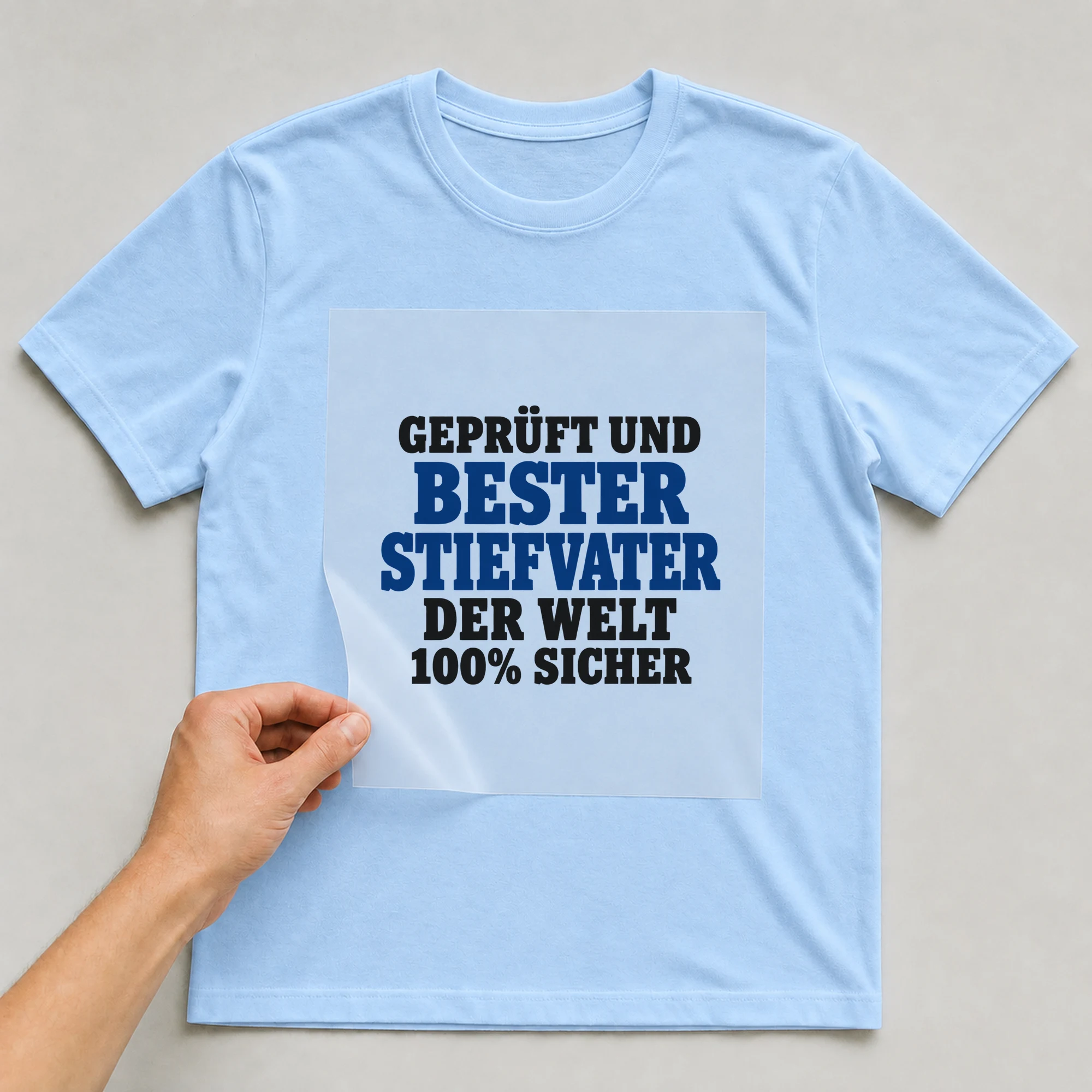 Bügelbild „Geprüft und bester Stiefvater der Welt 100% sicher“ auf babyblauem T-Shirt, Folie wird aufgelegt