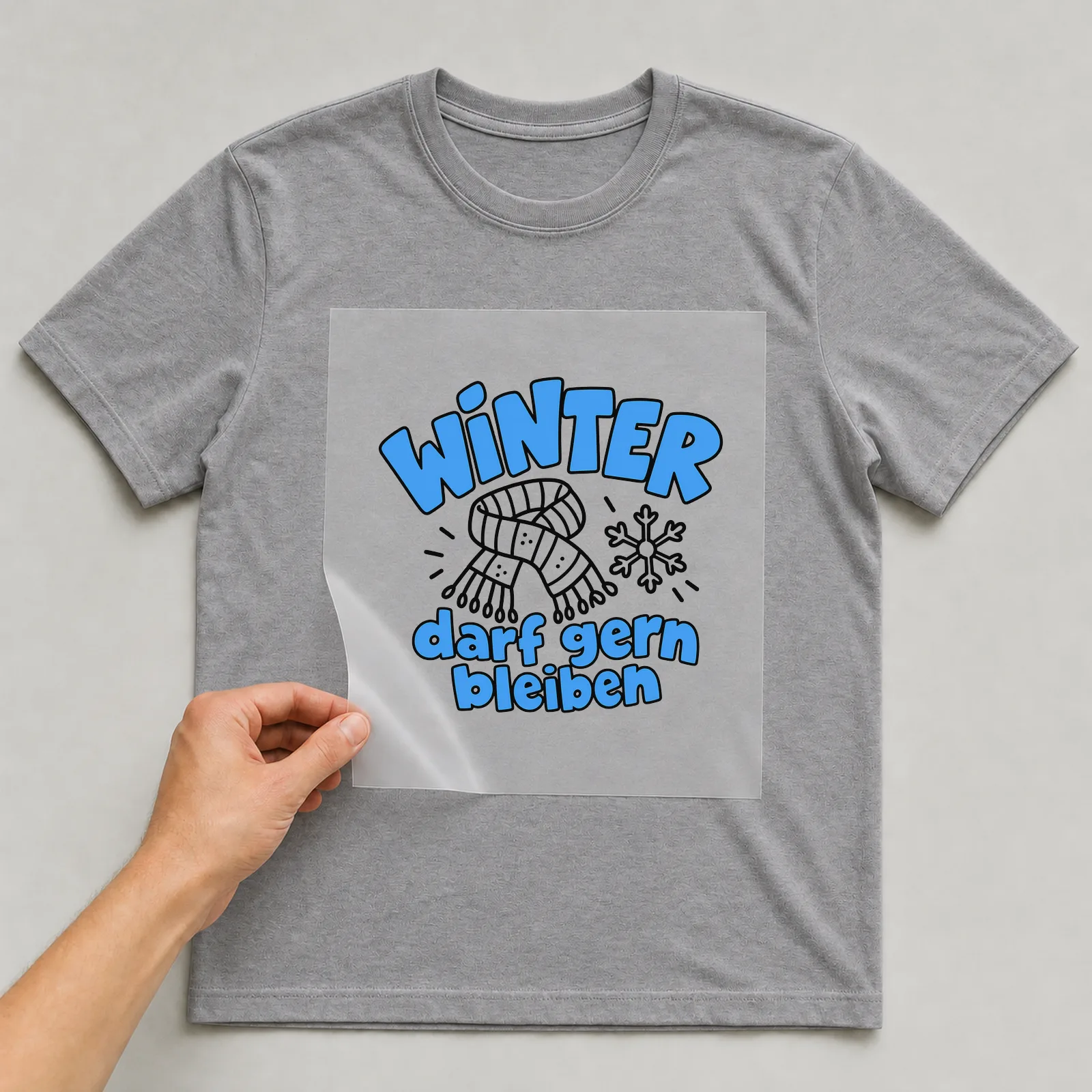 Bügelbild „Winter darf gern bleiben“ auf grauem T-Shirt, Folie wird aufgelegt