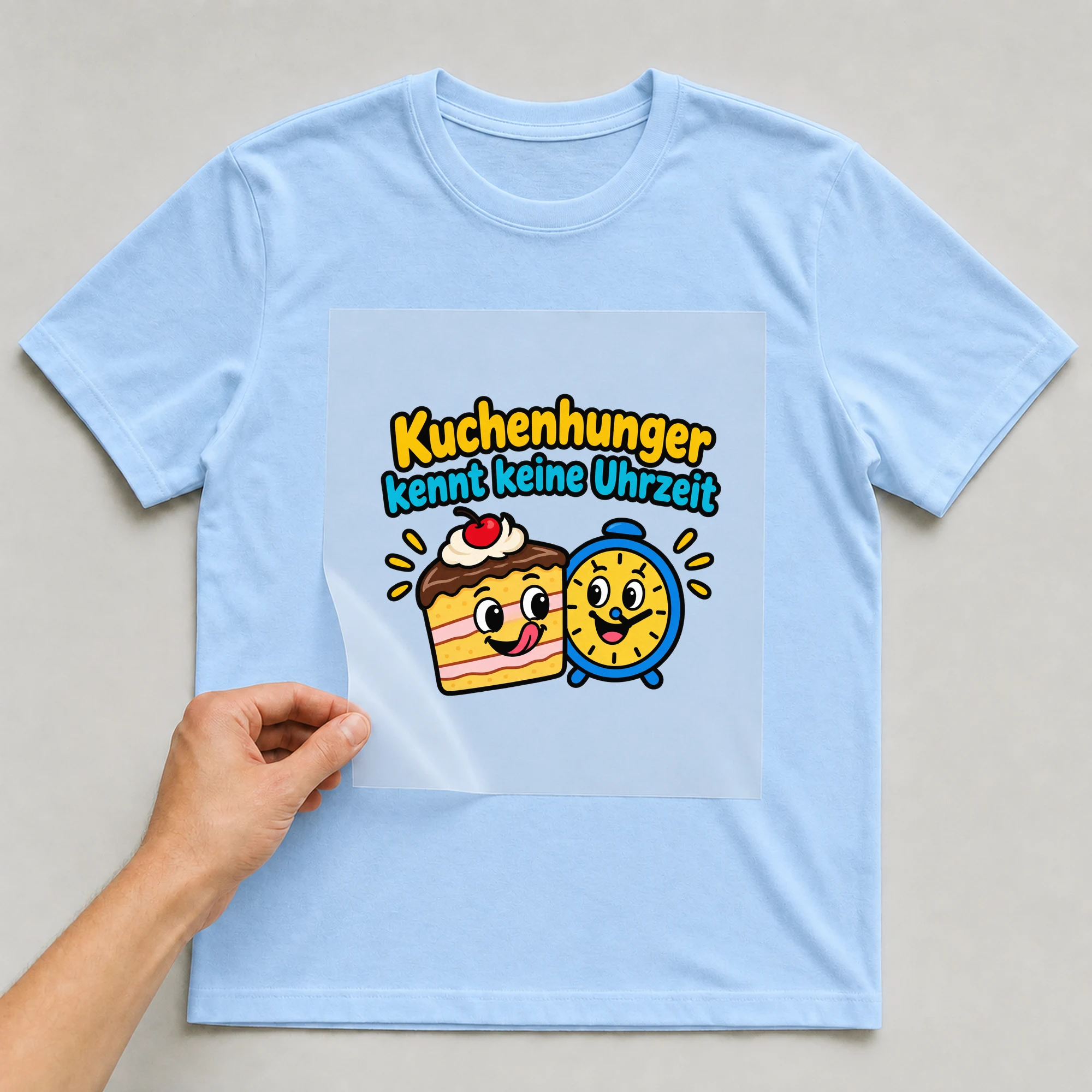 Bügelbild „Kuchenhunger kennt keine Uhrzeit“ auf babyblauem T-Shirt, Folie wird aufgelegt