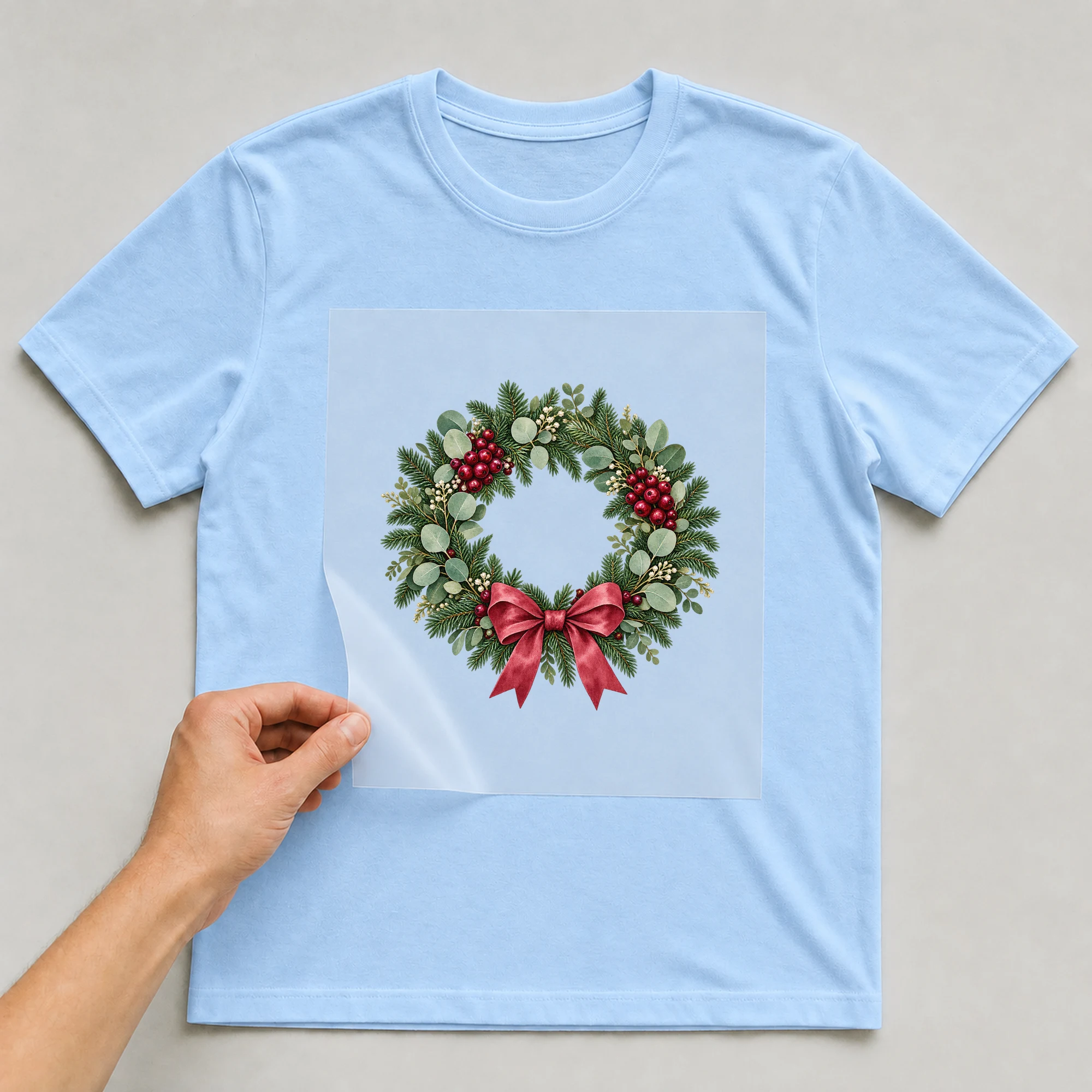 Bügelbild „Weihnachtskranz“ auf babyblauem T-Shirt, Folie wird aufgelegt