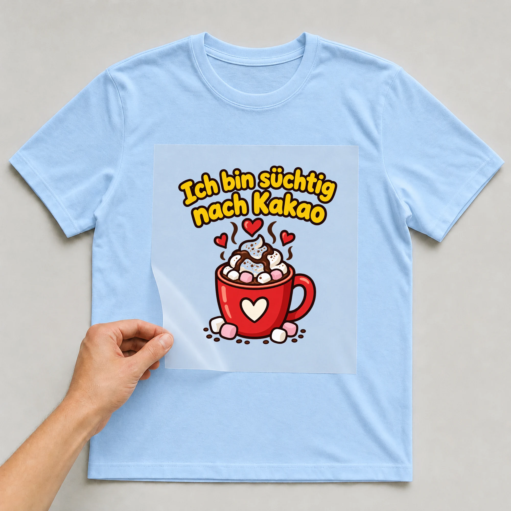 Bügelbild „Ich bin süchtig nach Kakao“ auf babyblauem T-Shirt, Folie wird aufgelegt