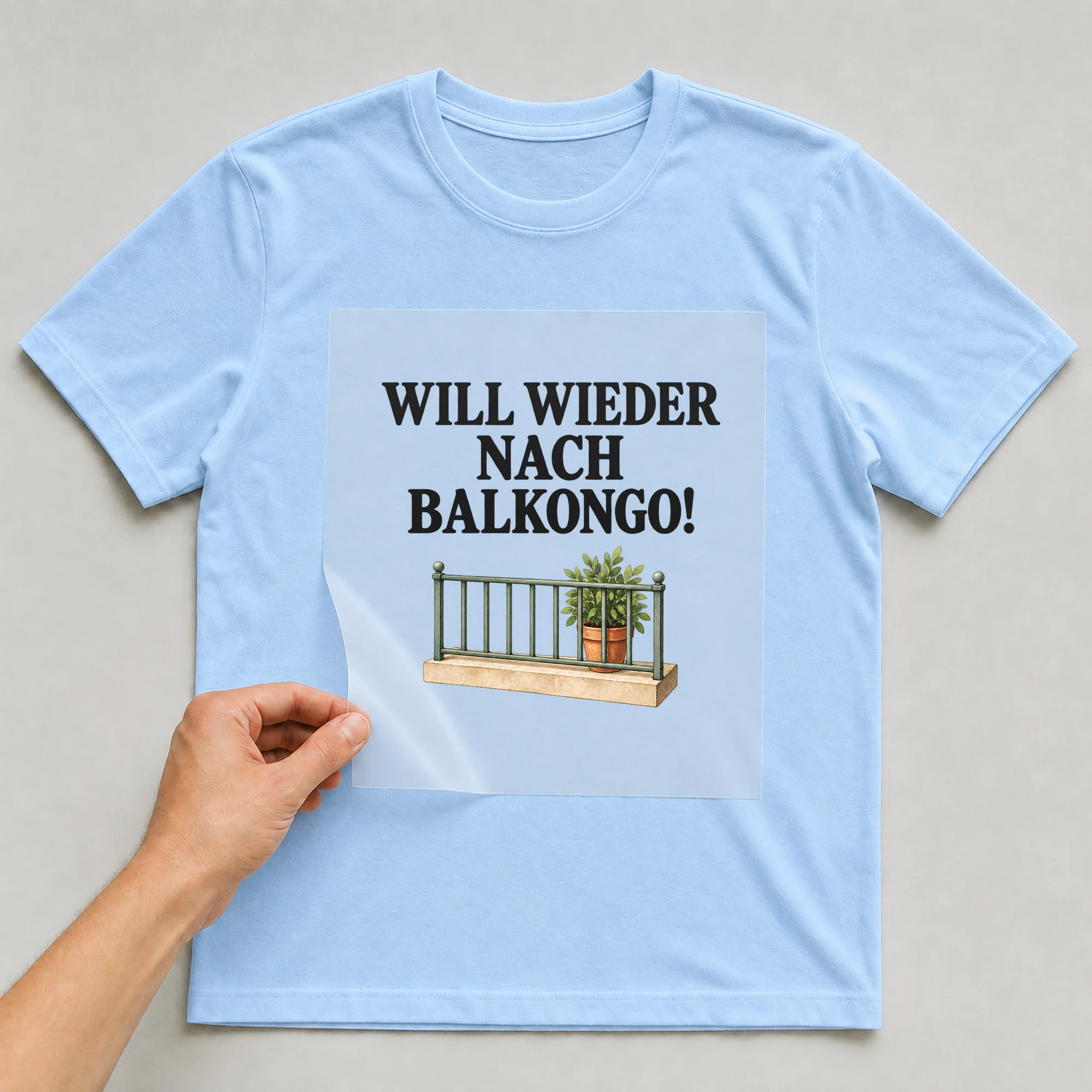 Bügelbild „WILL WIEDER NACH BALKONGO!“ auf babyblauem T-Shirt, Folie wird aufgelegt