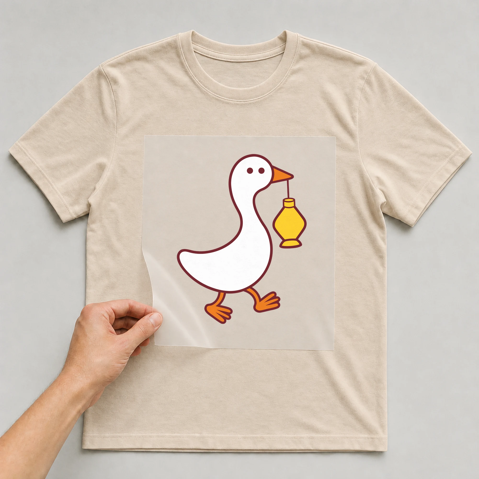 Bügelbild „Gans mit Laterne“ auf beigem T-Shirt, Folie wird aufgelegt