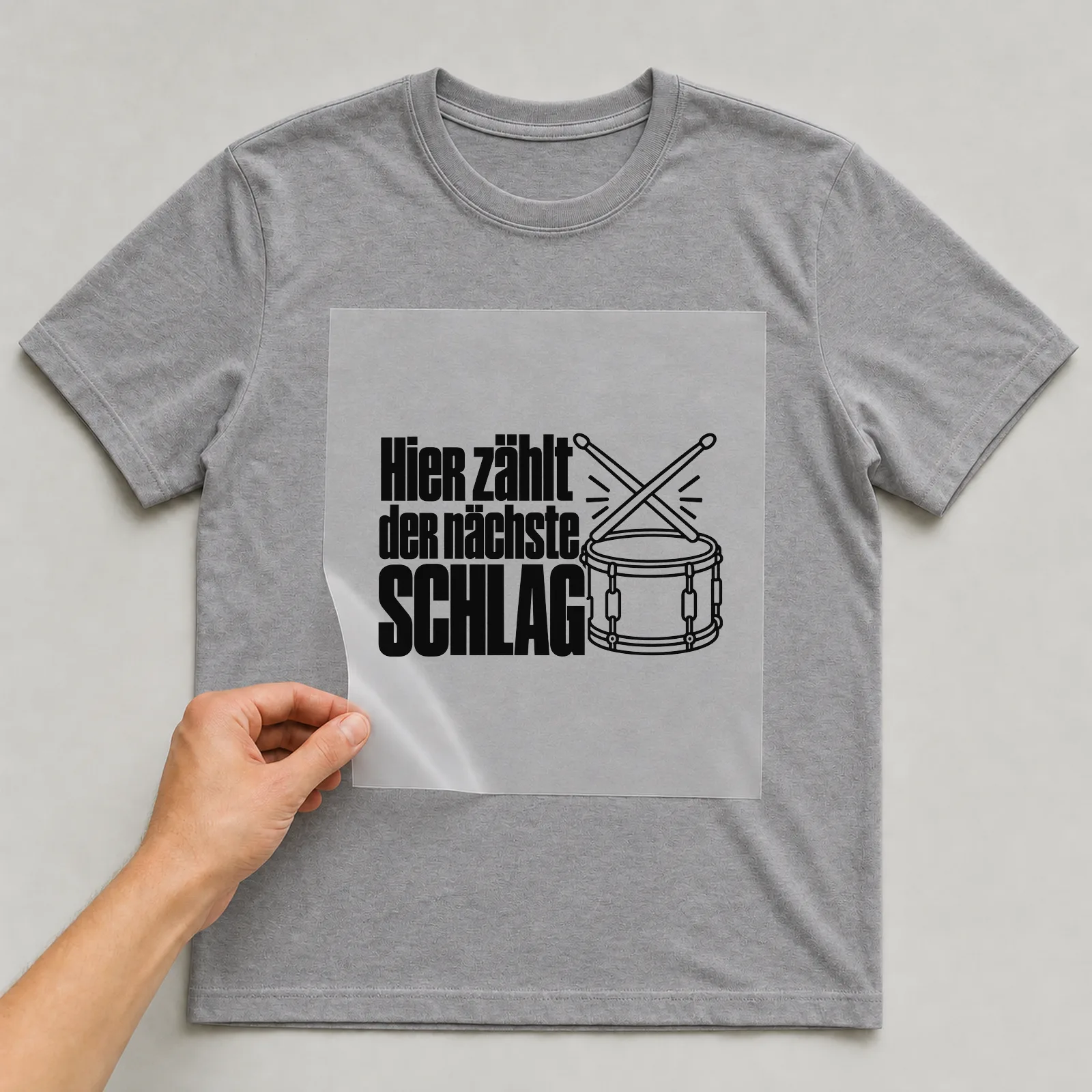 Bügelbild „Hier zählt der nächste Schlag“ auf grauem T-Shirt, Folie wird aufgelegt