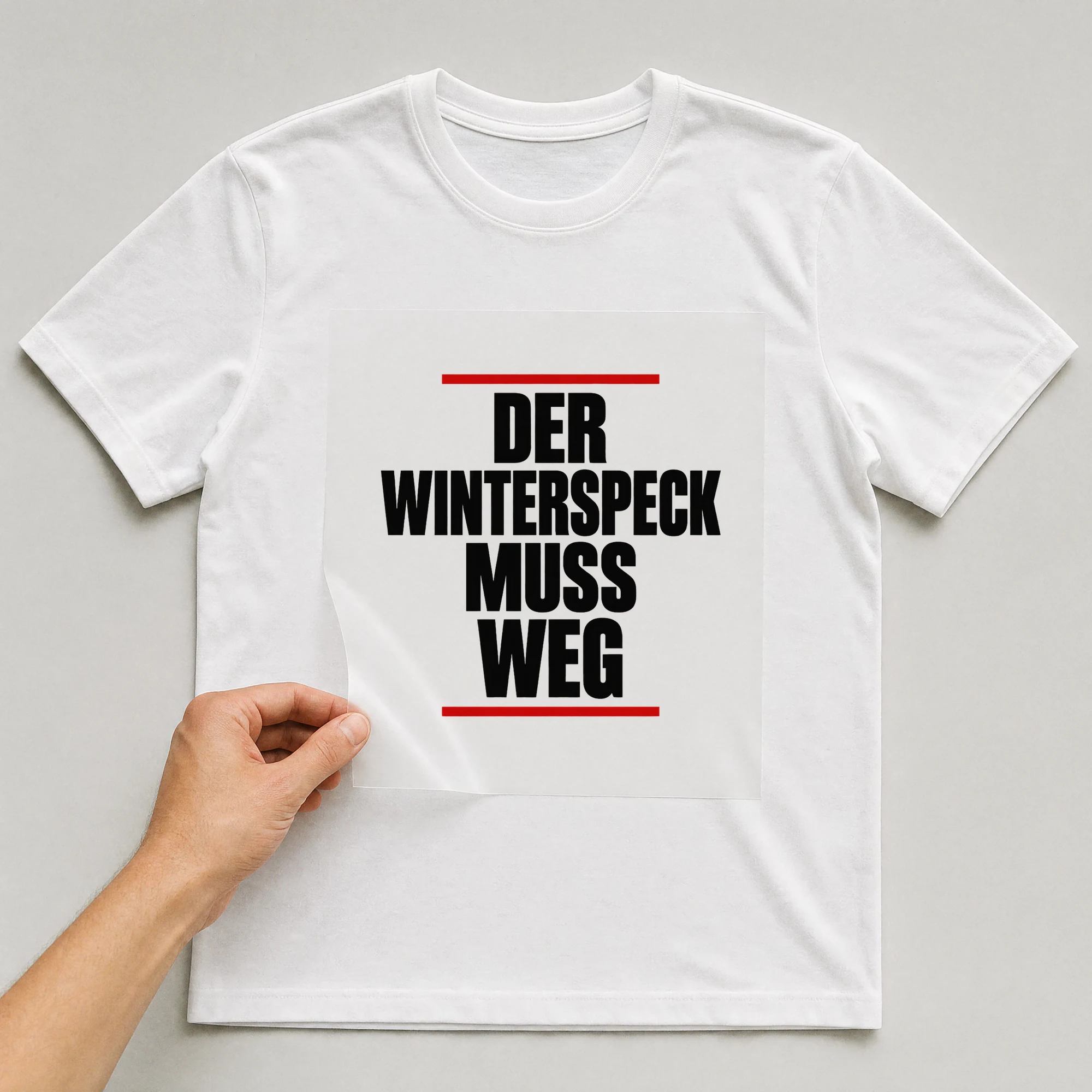 Bügelbild „Der Winterspeck muss weg“ auf weißem T-Shirt, Folie wird aufgelegt