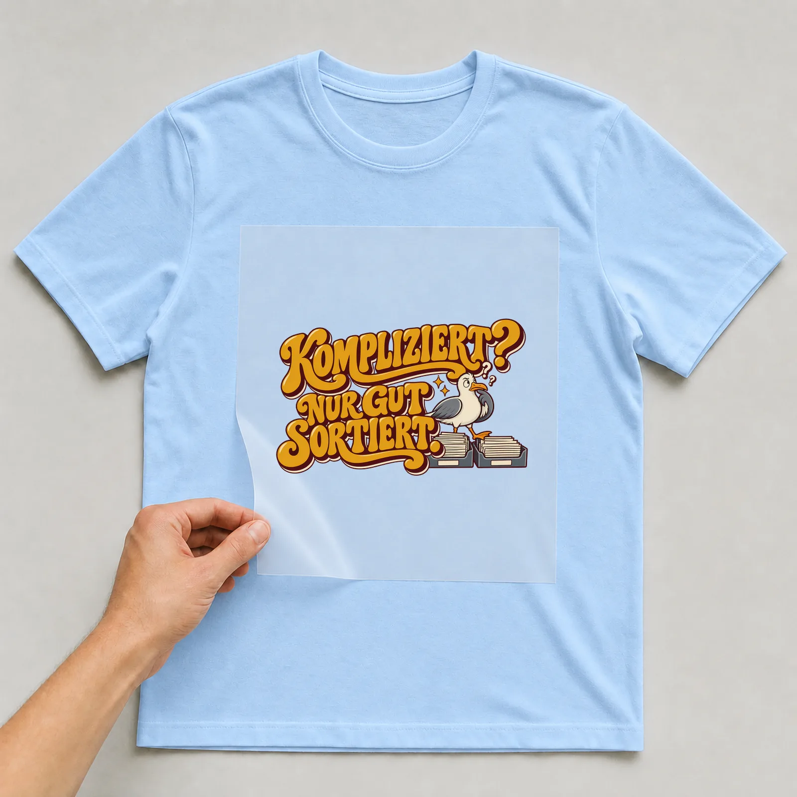 Bügelbild „Kompliziert? Nur gut sortiert.“ auf hellblauem T-Shirt, Folie wird aufgelegt
