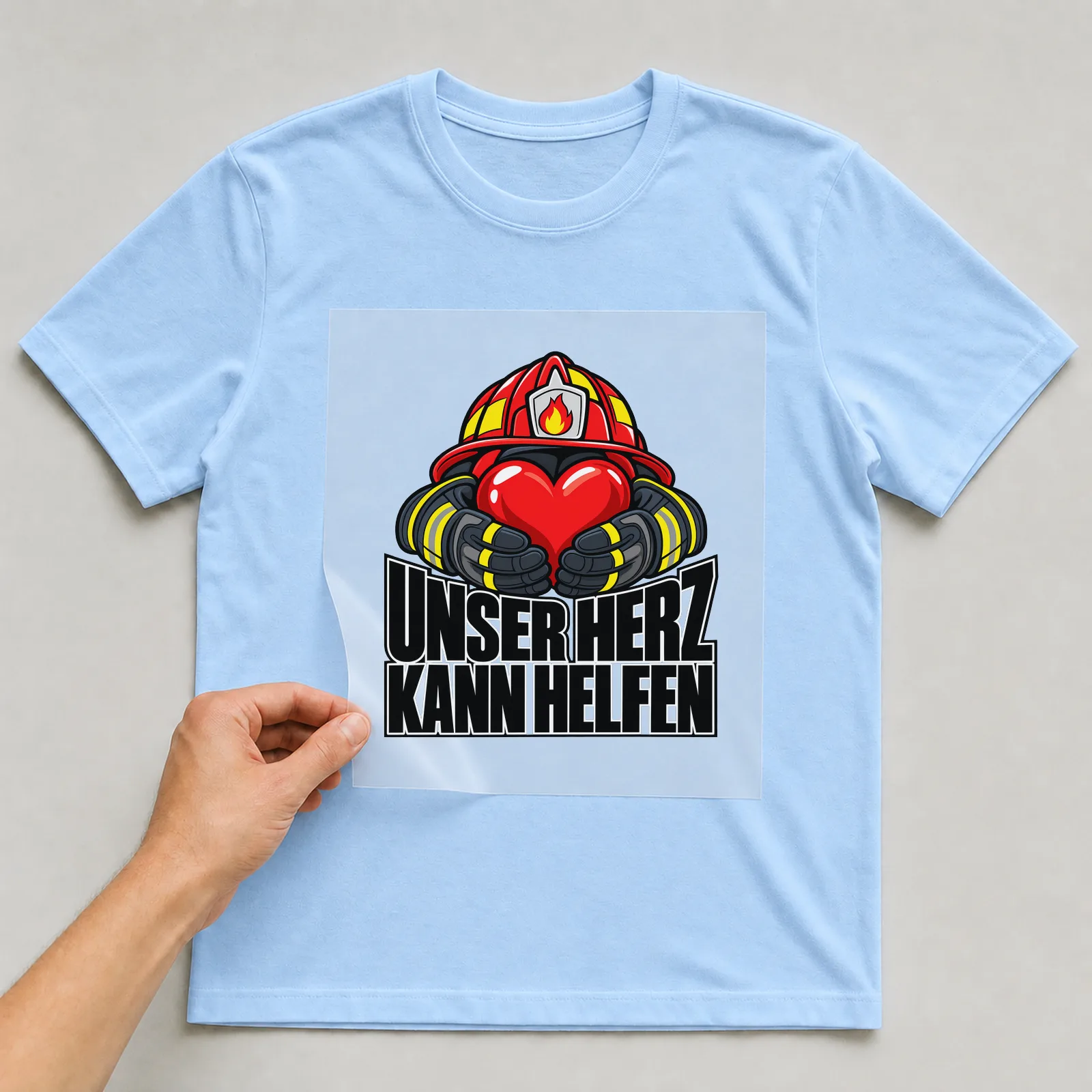 Bügelbild „Unser Herz kann helfen“ auf hellblauem T-Shirt, Folie wird aufgelegt