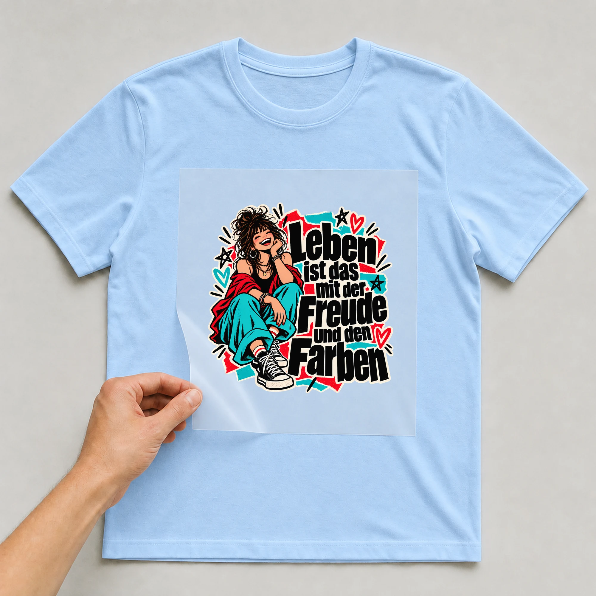 Bügelbild „Leben ist das mit der Freude und den Farben“ auf babyblauem T-Shirt, Folie wird aufgelegt