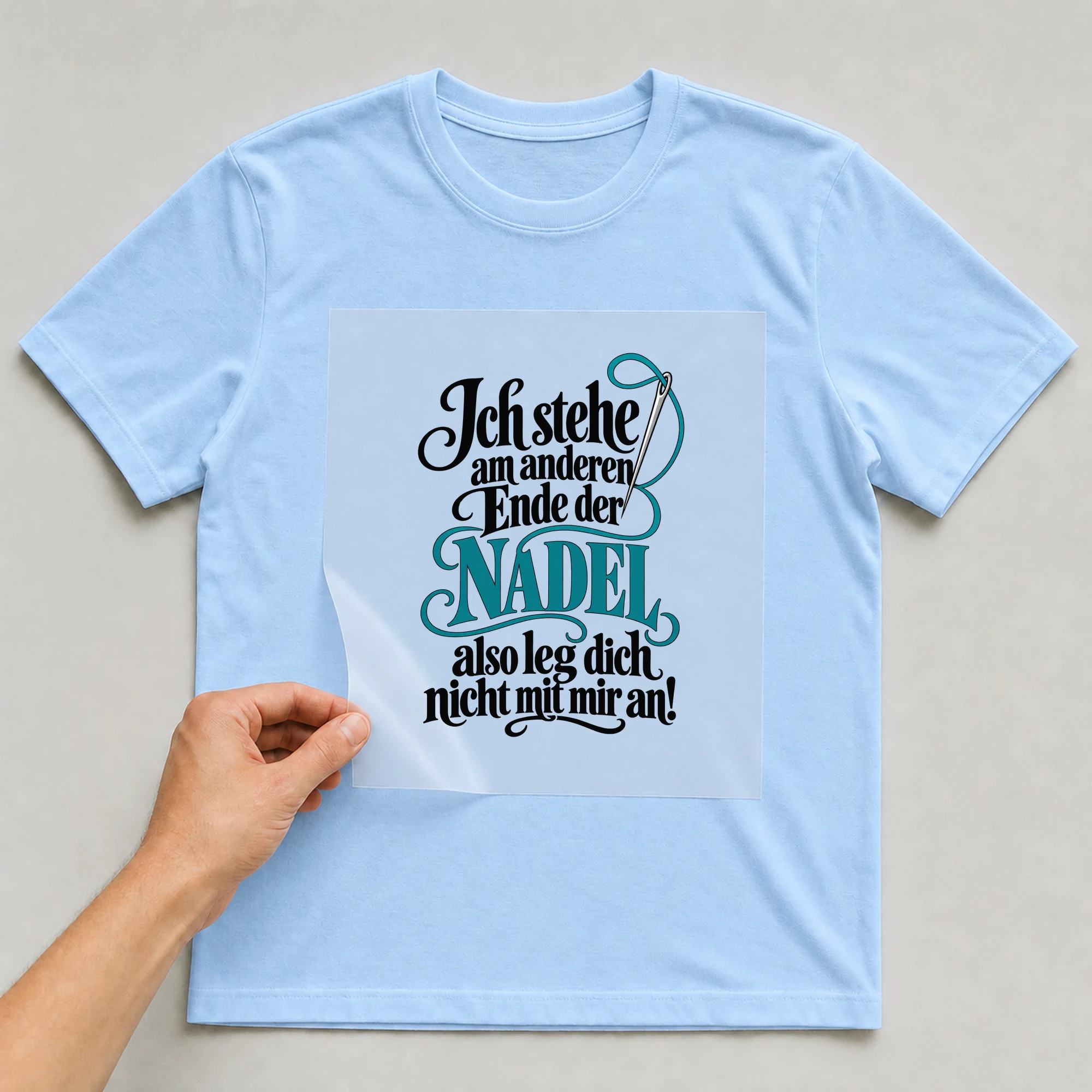 Bügelbild „Ich stehe am anderen Ende der NADEL also leg dich nicht mit mir an!“ auf babyblauem T-Shirt, Folie wird aufgelegt