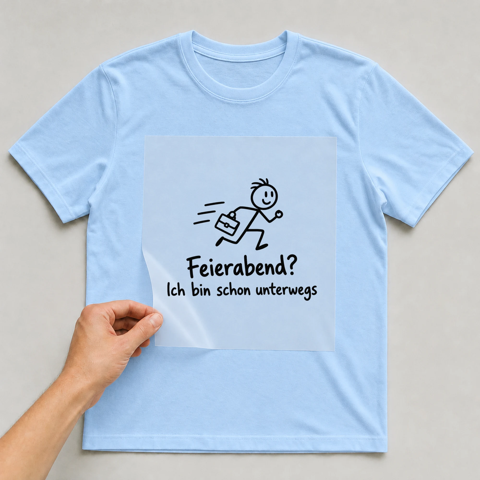 Bügelbild „Feierabend? Ich bin schon unterwegs“ auf babyblauem T-Shirt, Folie wird aufgelegt