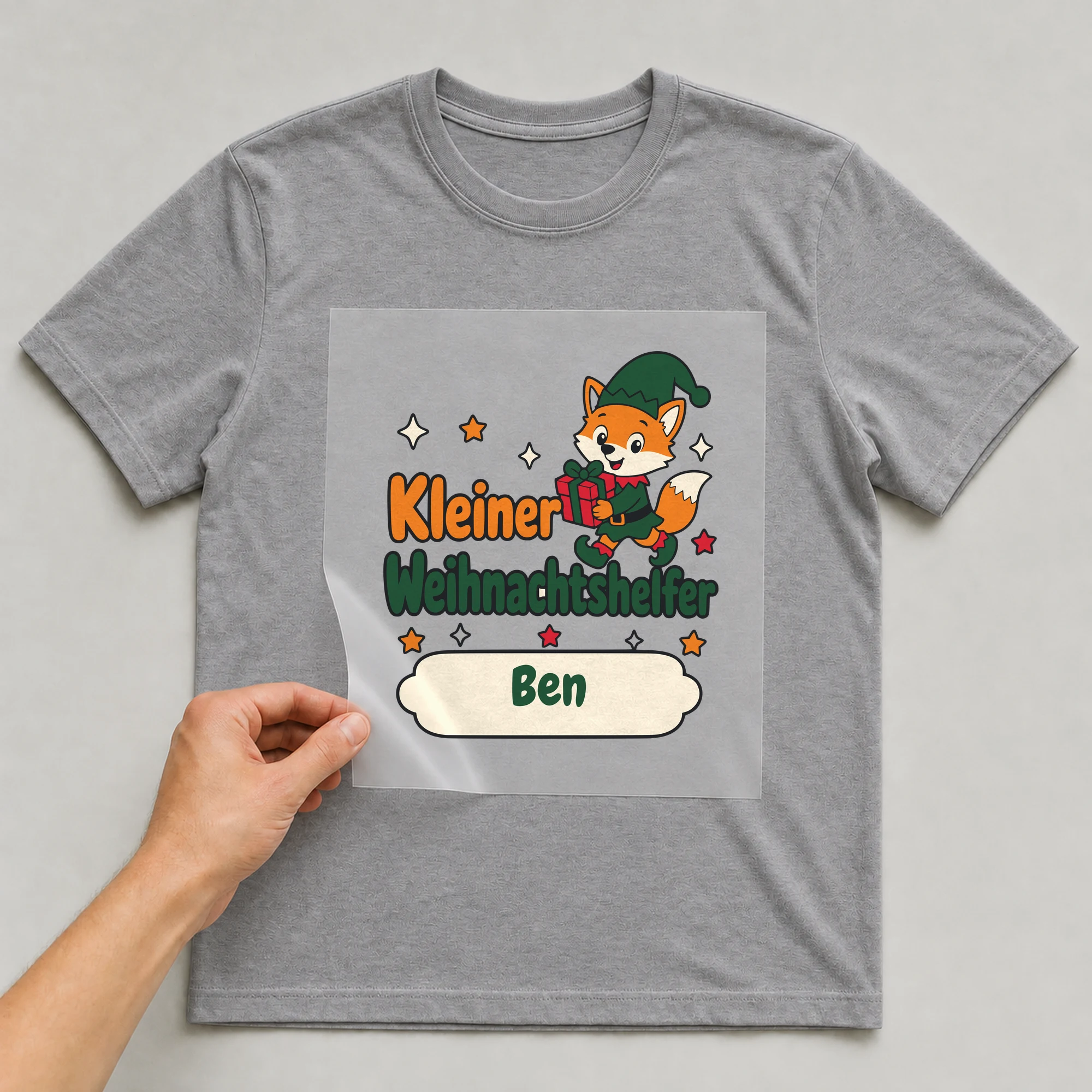 Bügelbild Kleiner Weihnachtshelfer mit Name auf grauem T-Shirt, Folie wird aufgelegt