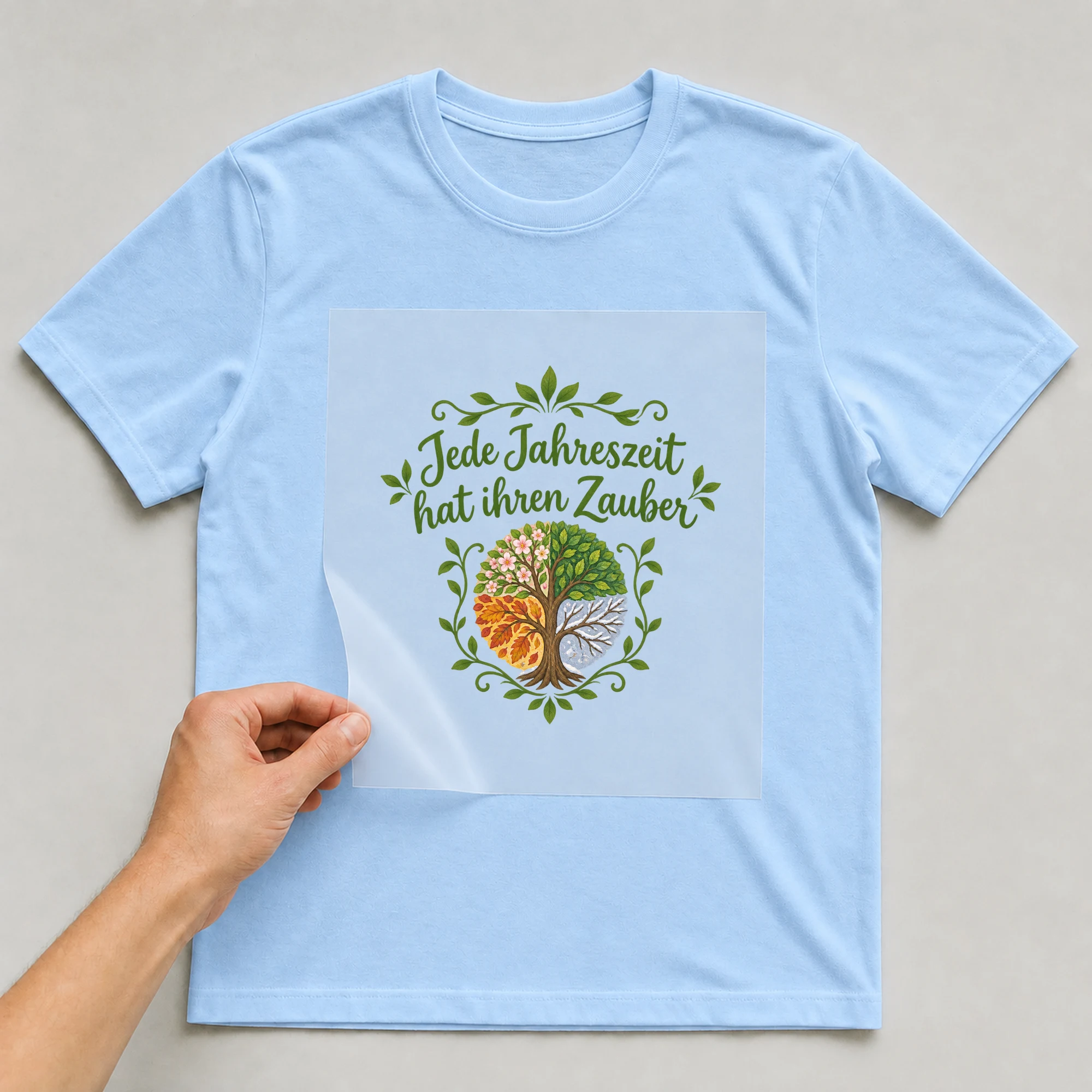 Bügelbild „Jede Jahreszeit hat ihren Zauber“ auf babyblauem T-Shirt, Folie wird aufgelegt