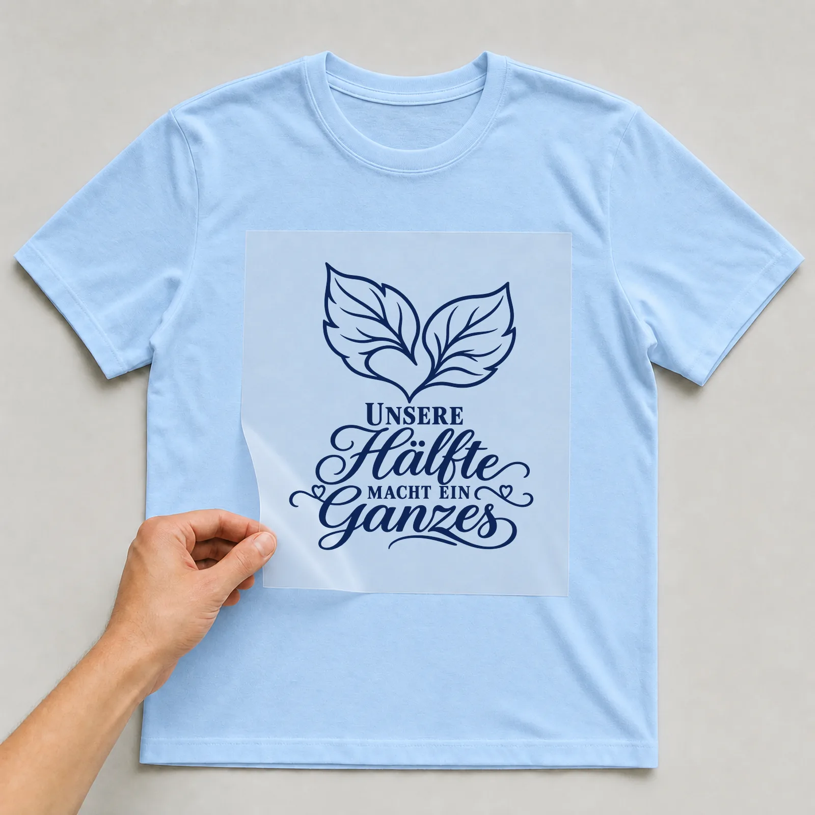 Bügelbild „Unsere Hälfte macht ein Ganzes“ auf hellblauem T-Shirt, Folie wird aufgelegt