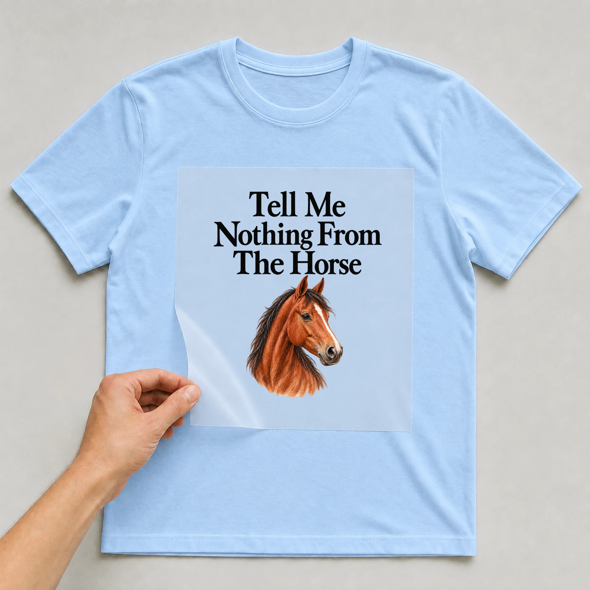 Bügelbild „Tell Me Nothing From The Horse“ auf babyblauem T-Shirt, Folie wird aufgelegt
