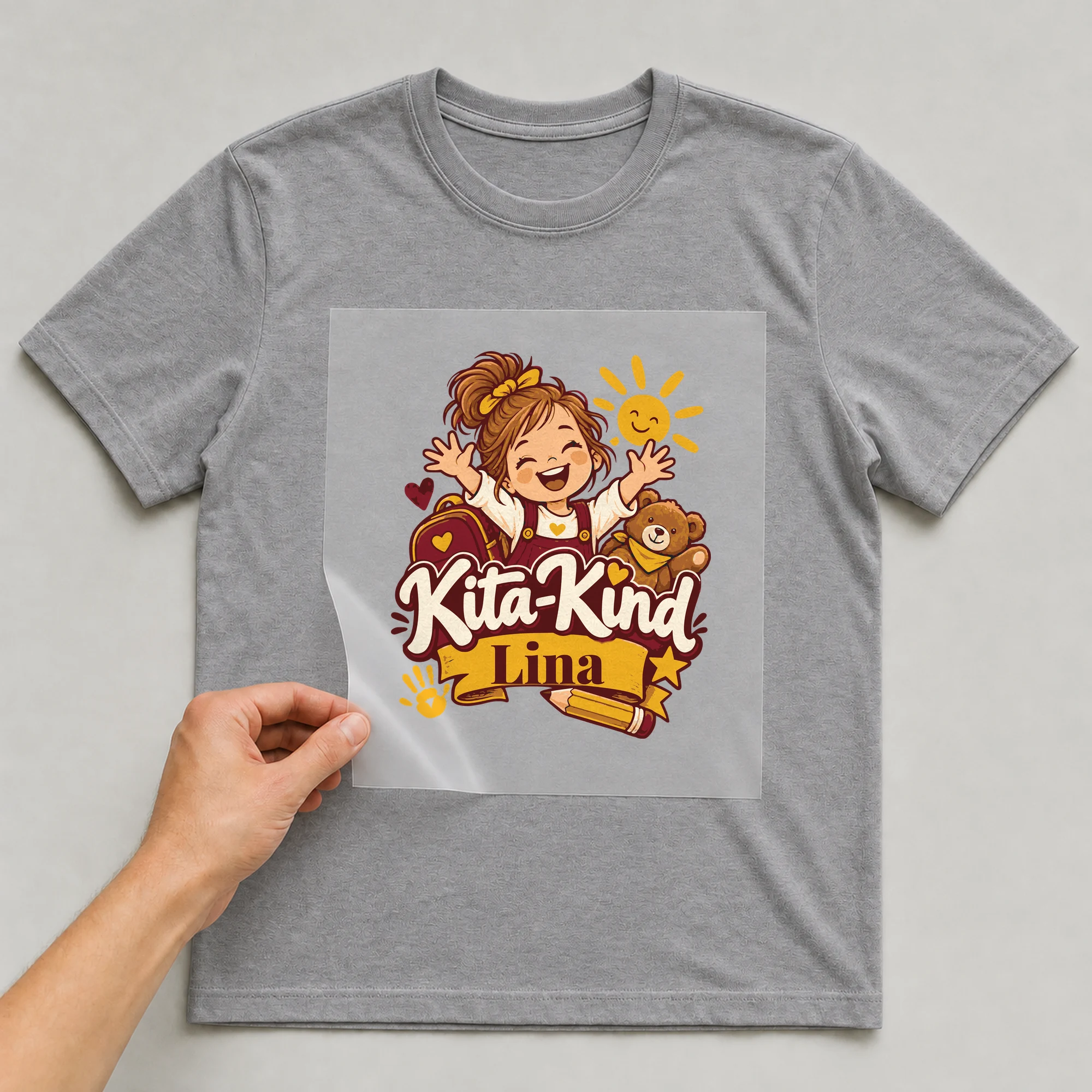 Bügelbild Kita-Kind mit Name auf grauem T-Shirt, Folie wird aufgelegt