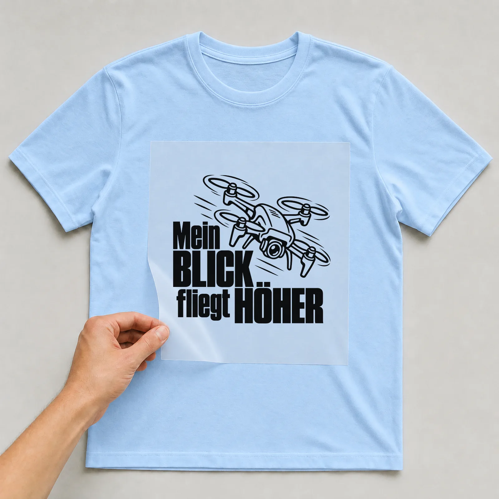 Bügelbild „Mein Blick fliegt höher“ auf hellblauem T-Shirt, Folie wird aufgelegt
