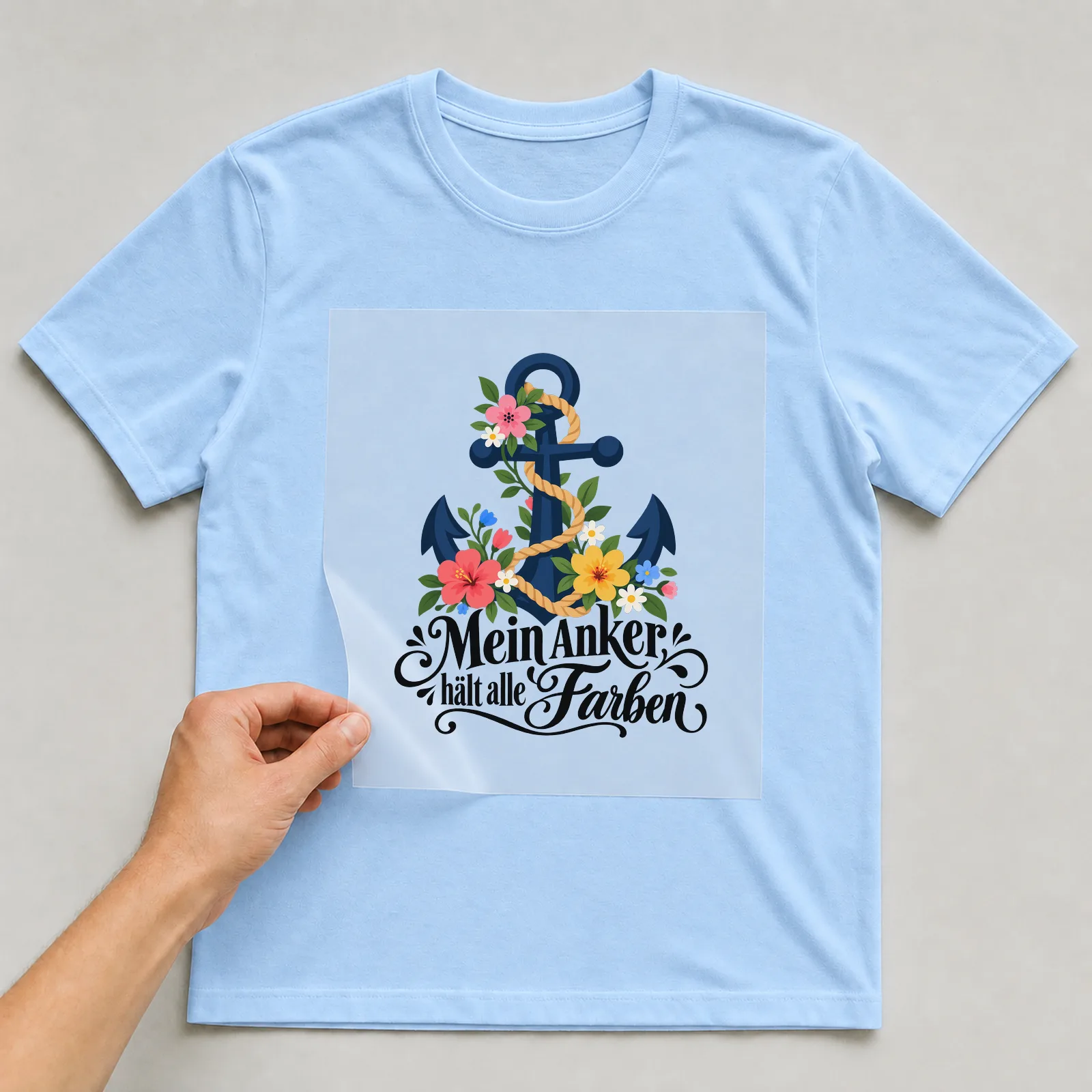 Bügelbild „Mein Anker hält alle Farben“ auf hellblauem T-Shirt, Folie wird aufgelegt