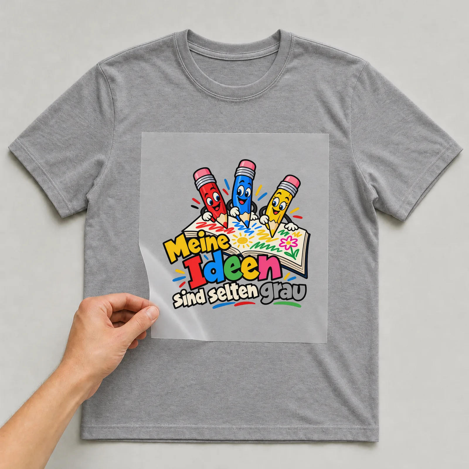 Bügelbild „Meine Ideen sind selten grau“ auf grauem T-Shirt, Folie wird aufgelegt