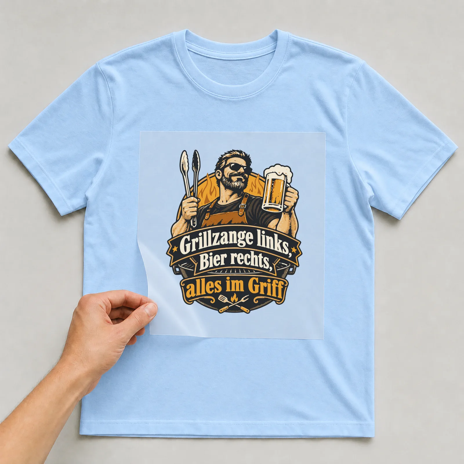 Bügelbild Grillzange links, Bier rechts, alles im Griff auf hellblauem T-Shirt, Folie wird aufgelegt