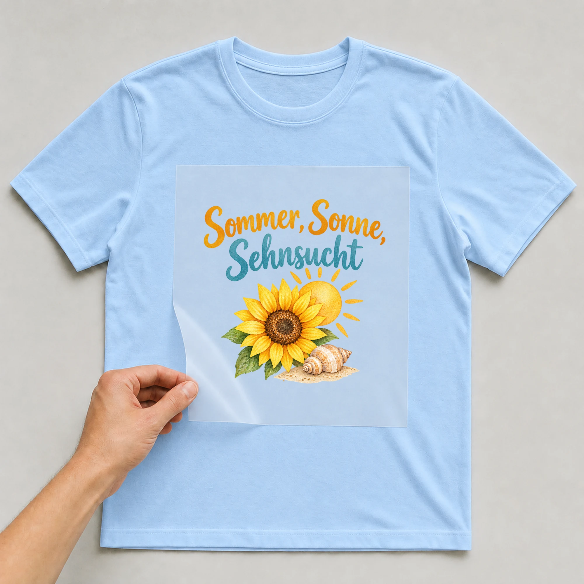 Bügelbild „Sommer, Sonne, Sehnsucht“ auf babyblauem T-Shirt, Folie wird aufgelegt