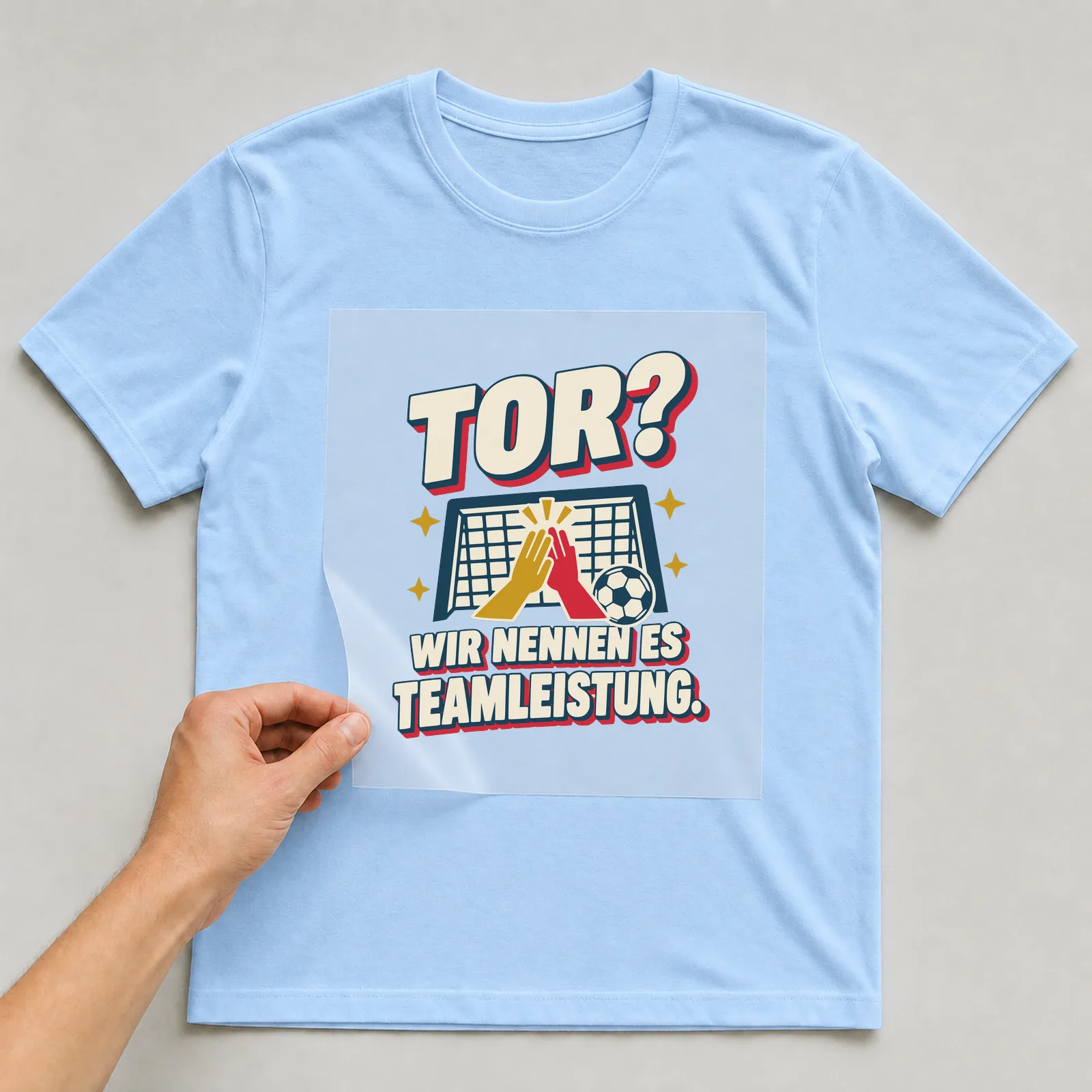Bügelbild Tor? Wir nennen es Teamleistung. auf hellblauem T-Shirt, Folie wird aufgelegt